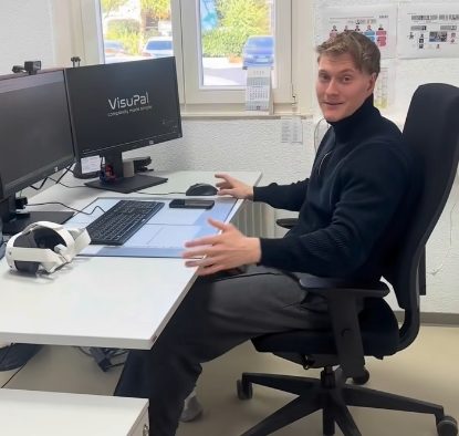 Teammitglied am Arbeitsplatz, auf dem Bildschirm das VisuPal-Logo, daneben eine VR-Brille auf dem Schreibtisch