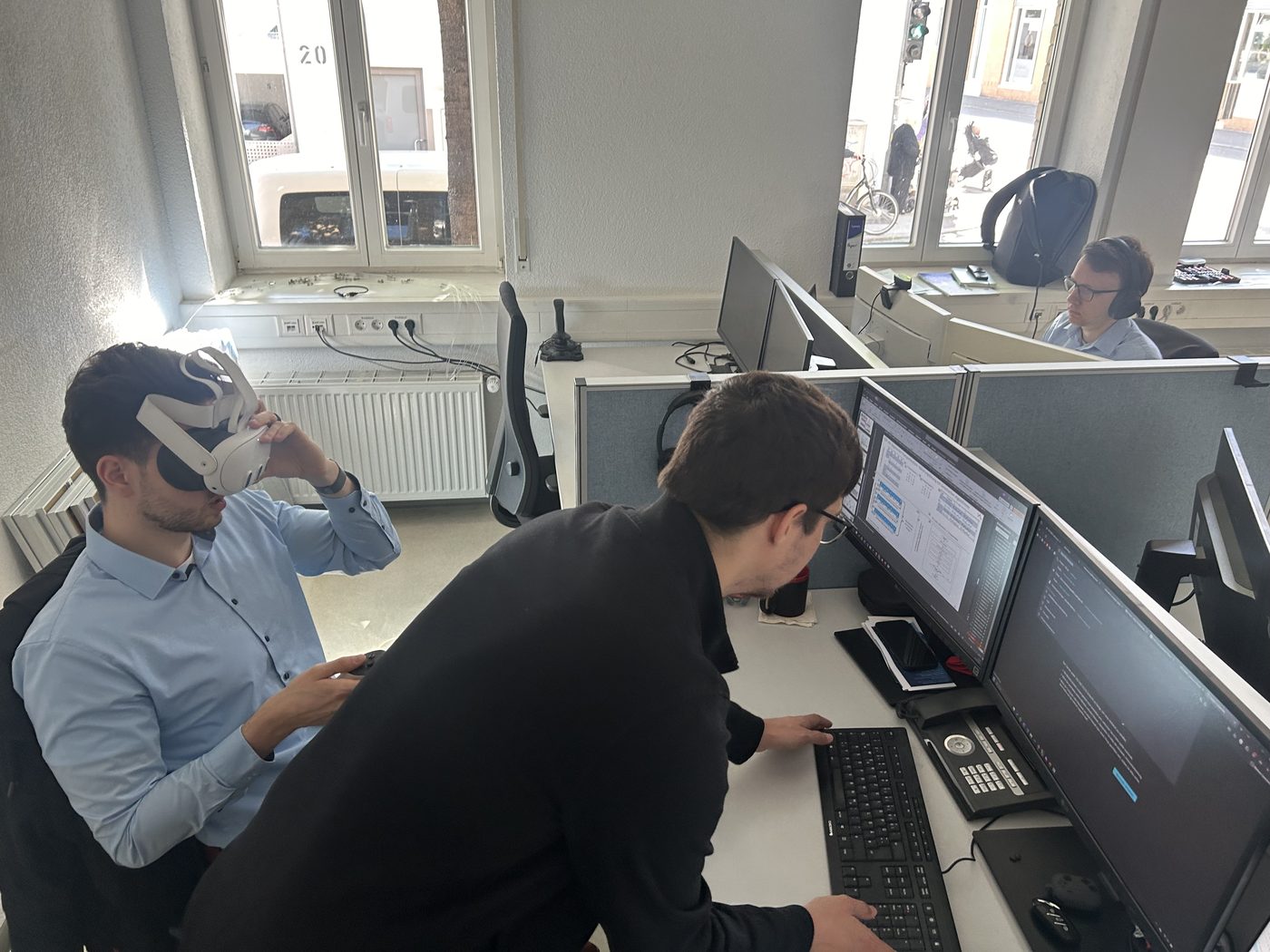 Ein Teammitglied testet am Arbeitsplatz eine VR-Brille, ein Kollege arbeitet daneben am Rechner